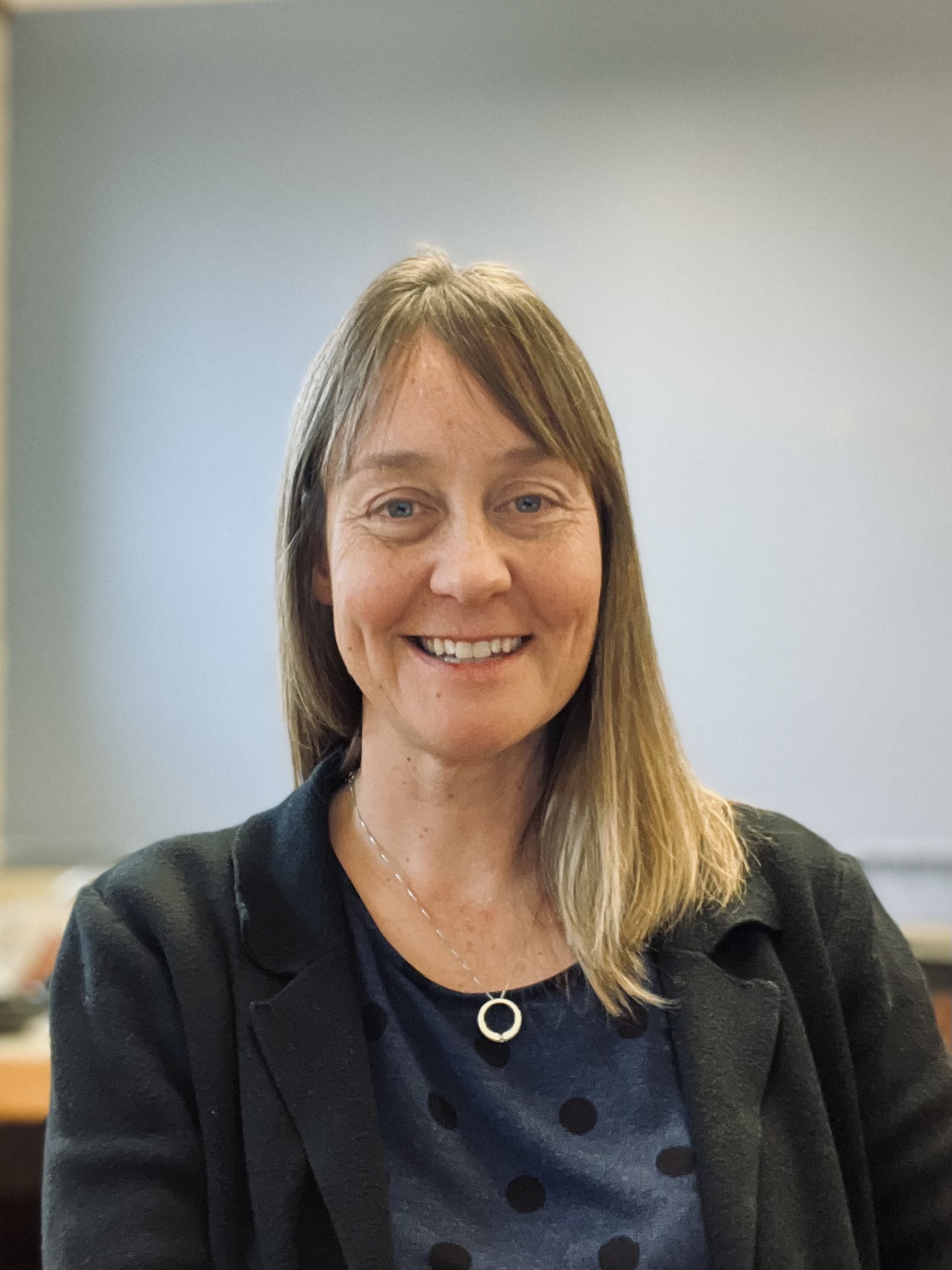 a woman with straight blonde hair wearing a blue top and black blazer