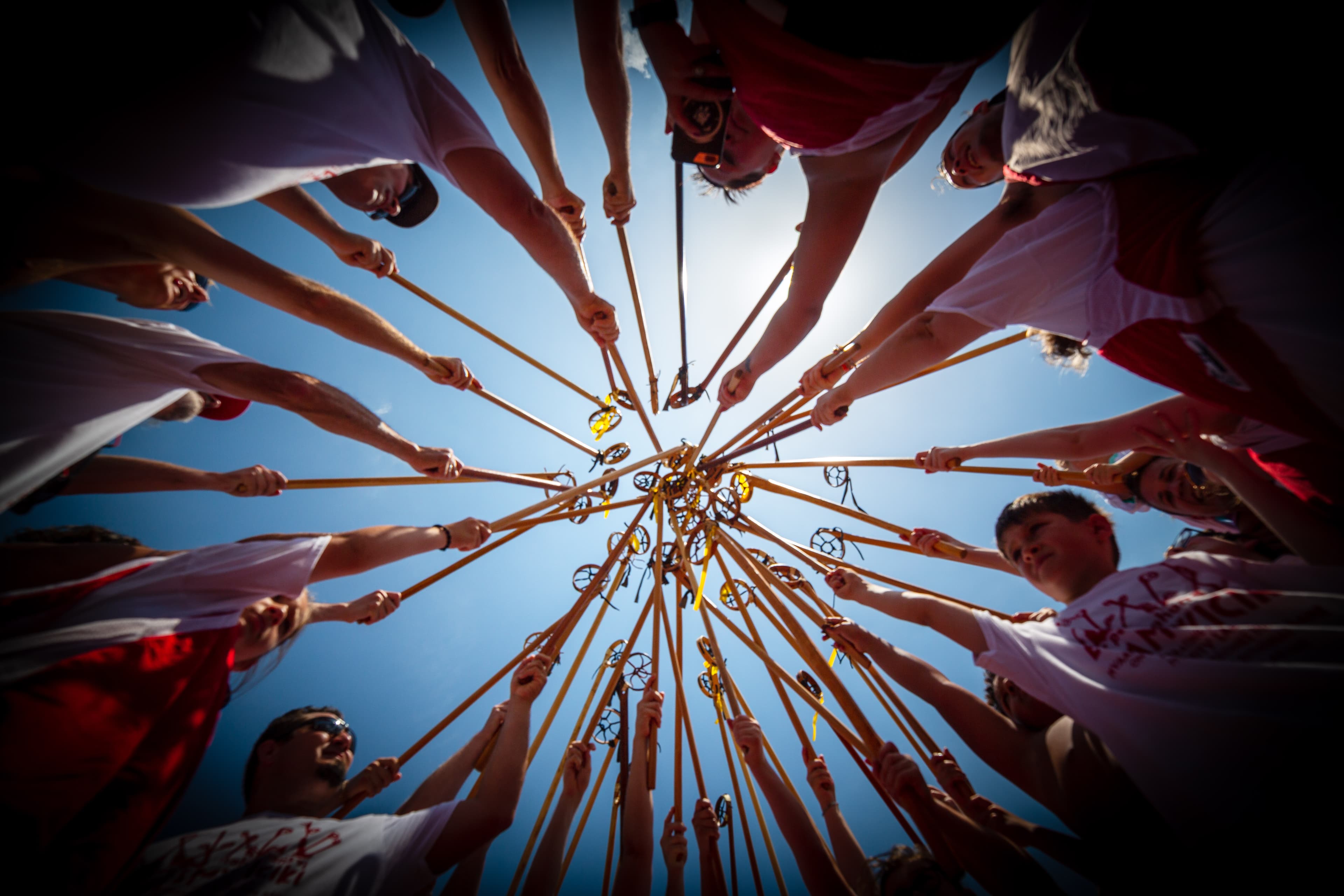 A group of lacrosse players in a circle, holding up their sticks towards the center.